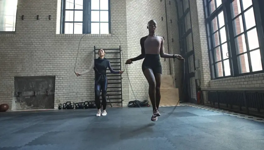 Dos mujeres realizan un calentamiento antes de hacer ejercicio, saltando la cuerda en un gimnasio industrial.