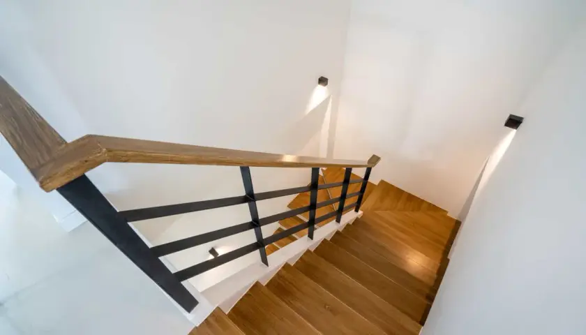 Nowoczesne oświetlenie klatki schodowej w domu jednorodzinnym, z drewnianymi stopniami i czarną balustradą.