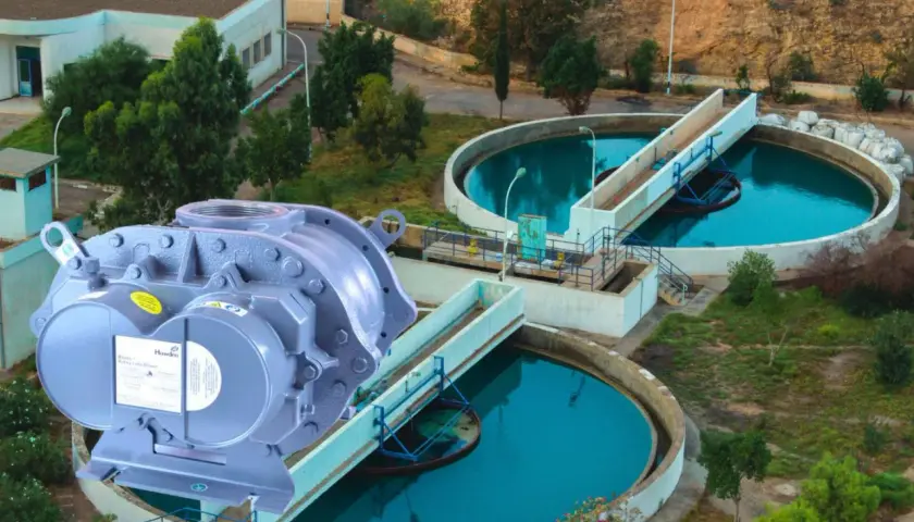 Un compresor de lóbulos Howden en primer plano, con una planta de tratamiento de agua al fondo.