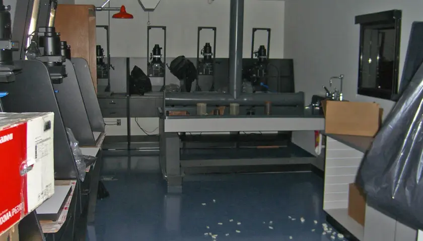 Wnętrze ciemni fotograficznej z kilkoma powiększalnikami, stołem laboratoryjnym i zlewem.