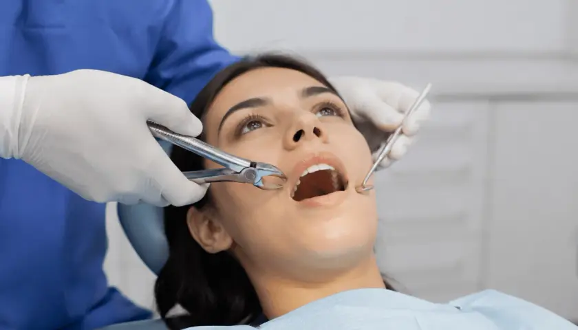Dentista usa fórceps para sacar muelas a paciente con boca abierta.