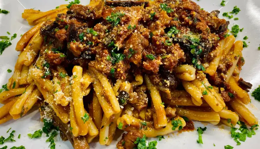 Un piatto di pasta alla norma fumante, con melanzane fritte, pomodoro e ricotta salata grattugiata, guarnito con prezzemolo fresco.
