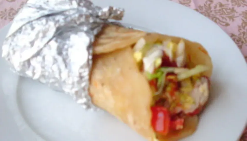 Pyszny placek z kebabem, zawinięty w folię aluminiową, z widocznym nadzieniem z warzyw i mięsa.