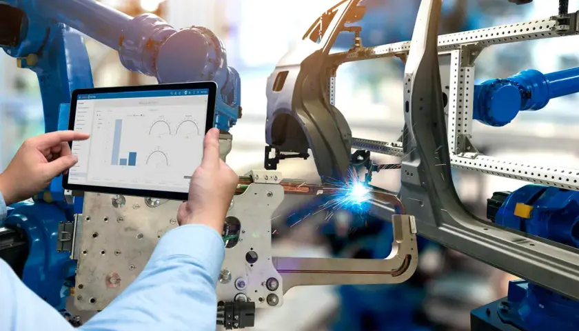Ein Roboter schweißt ein Autoteil, während ein Mensch auf einem Tablet die Produktionsdaten prüft. Was ist eine BOM? Hier wird sie digital verwaltet.