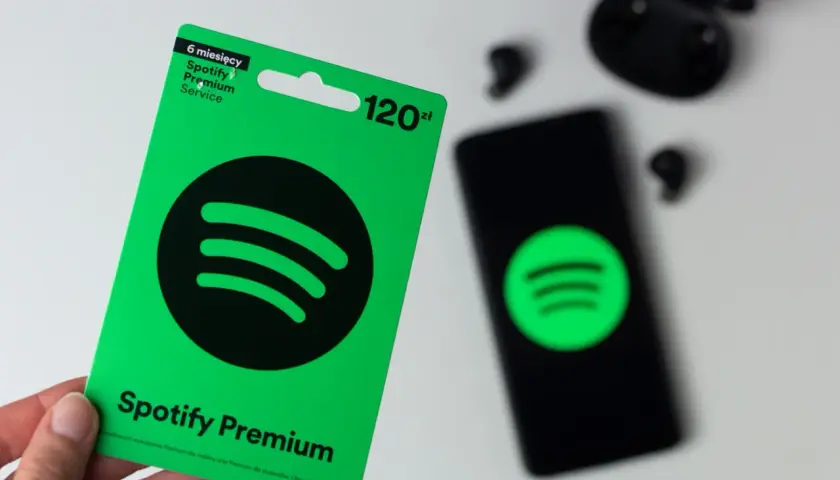 Karta podarunkowa Spotify Premium na 6 miesięcy kosztuje 120 zł. Obok leży smartfon z logo Spotify i słuchawki.