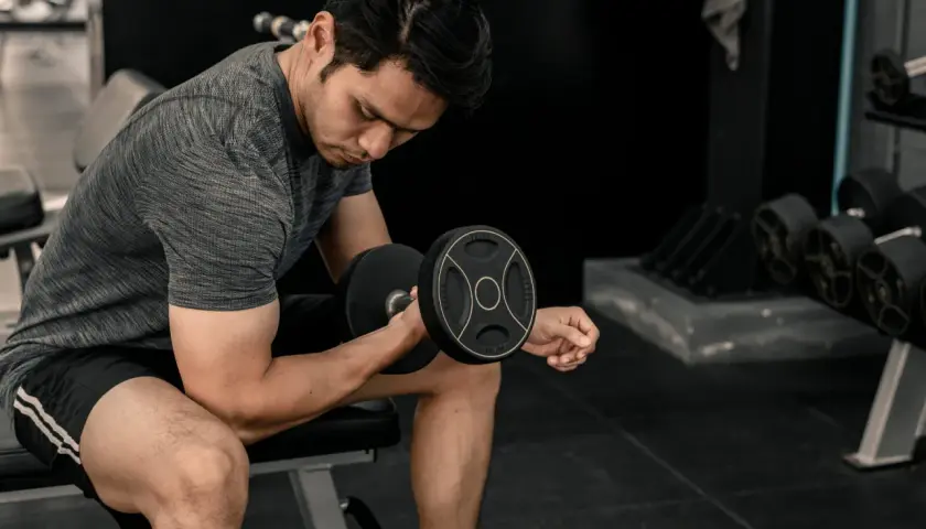 Mężczyzna ćwiczy biceps z hantlem. Energia do treningu pochodzi z glikogenu, który jest zapasem cukru w mięśniach.