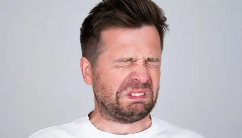 Mężczyzna z wykrzywioną twarzą, oczy zamknięte, czuje gorzki smak w ustach.