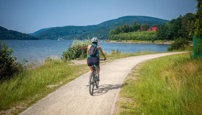 Kobieta na rowerze przemierza malowniczą ścieżkę nad jeziorem, odkrywając jedne z najlepszych tras rowerowych w Polsce.