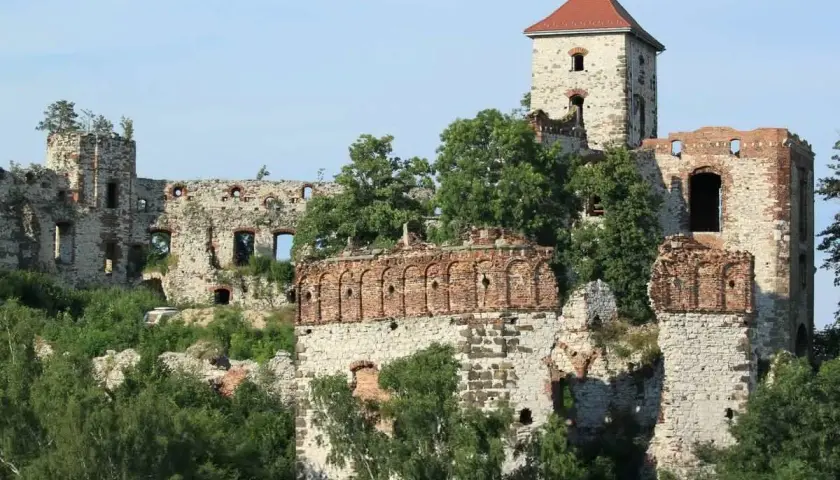 Ruiny zamku Tenczyn, kamienne mury i ceglane łuki porośnięte zielenią, z charakterystyczną wieżą pod czerwonym dachem.