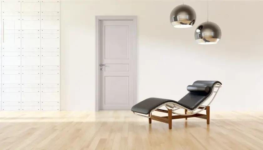 Un ambiente minimalista con porte bianche, pareti tortora, una chaise longue in pelle nera e due lampade a sospensione sferiche.