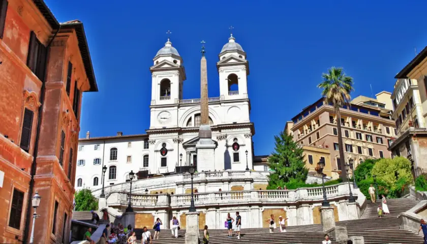 La scalinata di Trinità dei Monti a Roma, con la chiesa e l'obelisco sotto un cielo azzurro.
