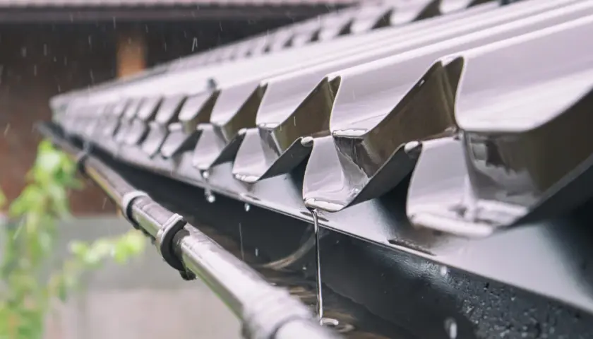 Deszcz spływa po metalowym dachu garażu, a mocowanie rynny do garażu blaszanego skutecznie odprowadza wodę.