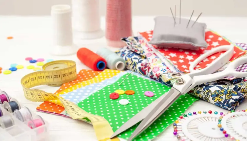A collection of 10 sewing tools: scissors, measuring tape, spools of thread, needles, buttons, and fabric scraps, ready for a creative project.