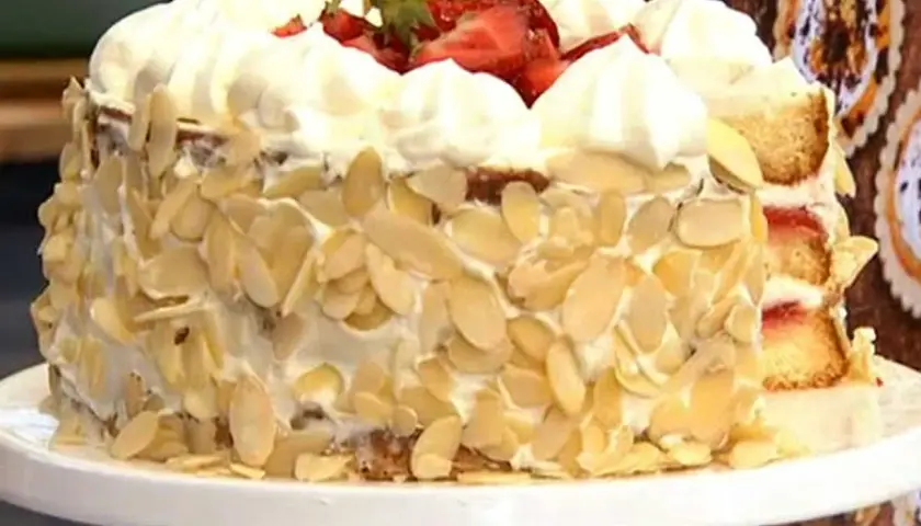 En vacker glutenfri jordgubbstårta täckt med vispgrädde och mandelspån, toppad med färska jordgubbar.