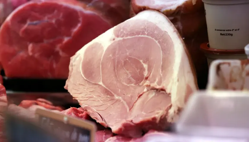 Gros plan sur une pièce de viande rose pâle, probablement une côte de porc, avec des marbrures de gras. Derrière, on aperçoit de la viande rouge vif.