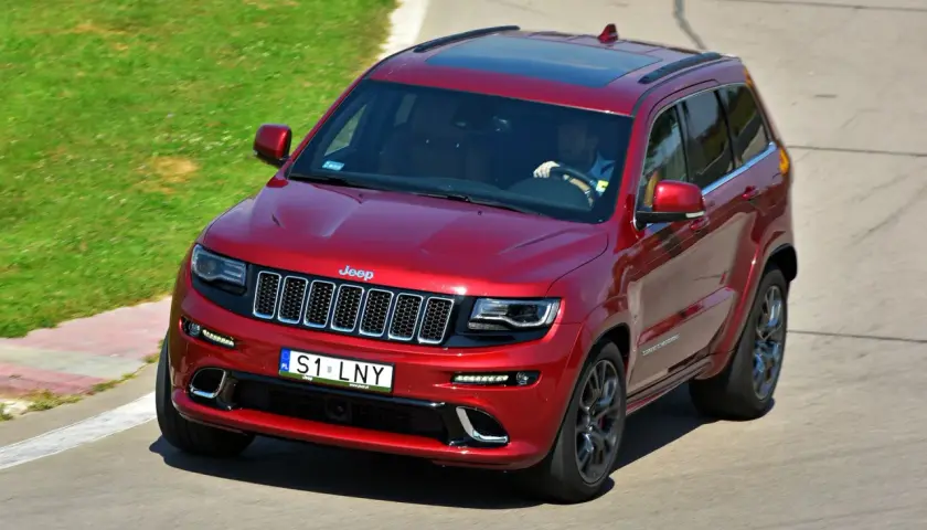 Czerwony Jeep Grand Cherokee z kierowcą za kierownicą, indywidualni na drodze, pokonuje zakręt na torze wyścigowym.
