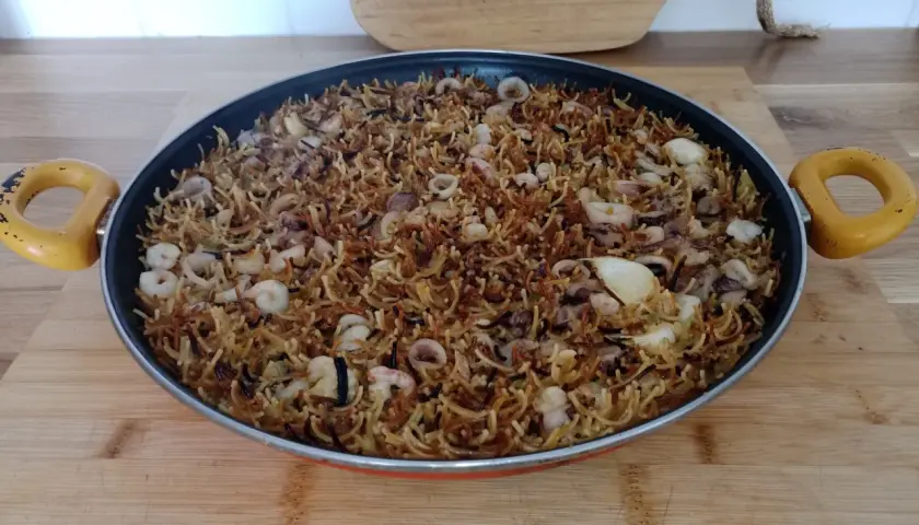 Fideos fideuá con calamares y gambas, listos para servir en una paellera.