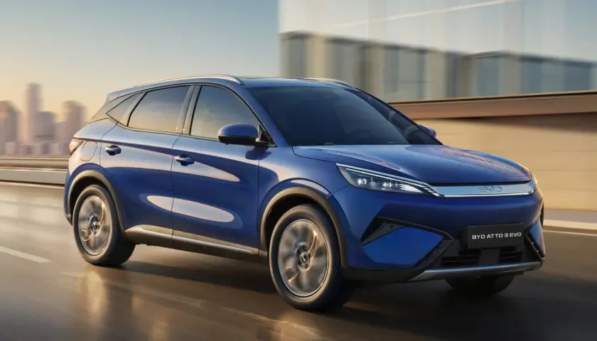 BYD Atto 3 blu in movimento, con la sua notevole autonomia, sfreccia su una strada urbana al tramonto.