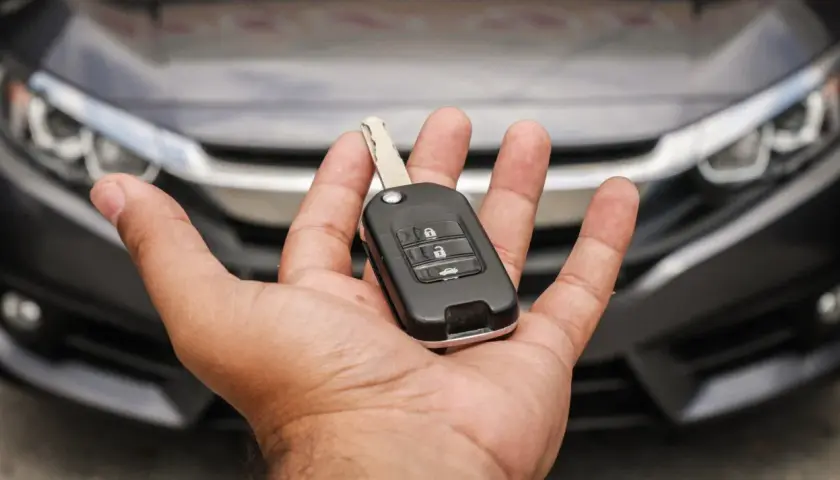 Mano che tiene una chiave auto moderna, pronta per duplicare la chiave auto. Auto scura sullo sfondo.