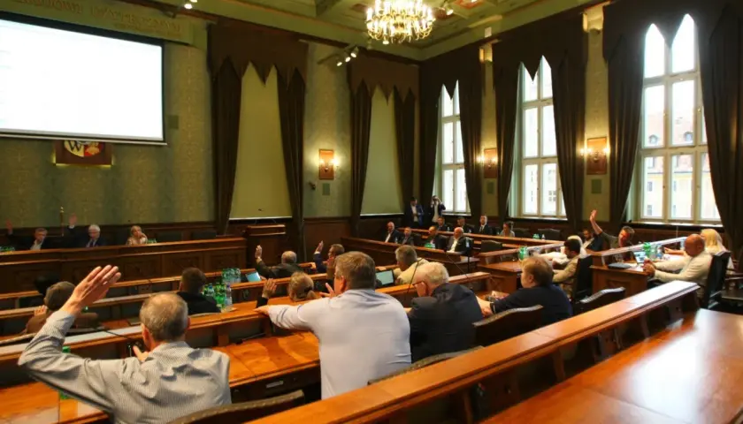 Sala obrad z ludźmi podnoszącymi ręce, widok zza pleców uczestników.