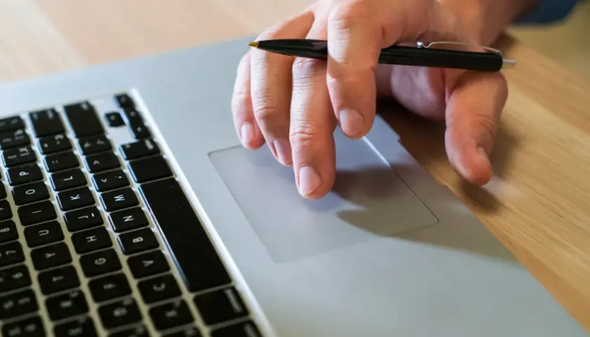 Mano con bolígrafo sobre el touchpad de un portátil, como si buscara qué es un hash.