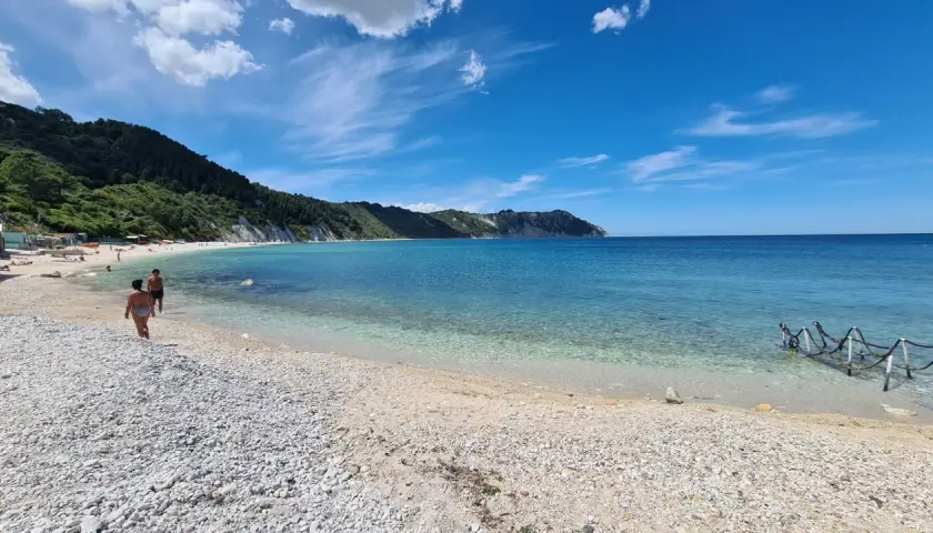 Spiaggia di Portonovo con il Monte Conero sullo sfondo. Acqua cristallina e cielo azzurro.