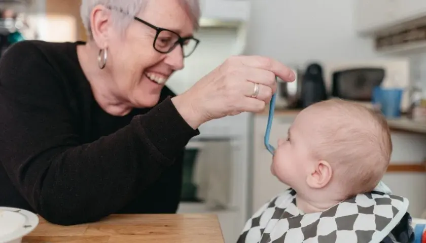 Glad mormor matar bebis med smakportioner. Första maten för en 4 månader gammal bebis.