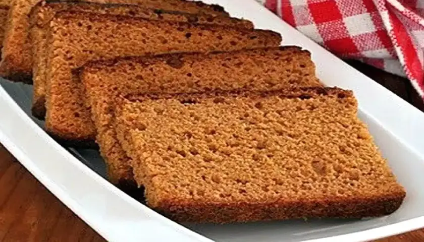 Tranches de pain d'épices moelleux disposées sur un plat blanc, avec un torchon à carreaux rouges en arrière-plan.