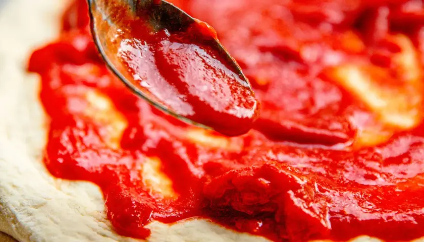 Cuchara esparciendo deliciosa salsa para pizza sobre la masa.