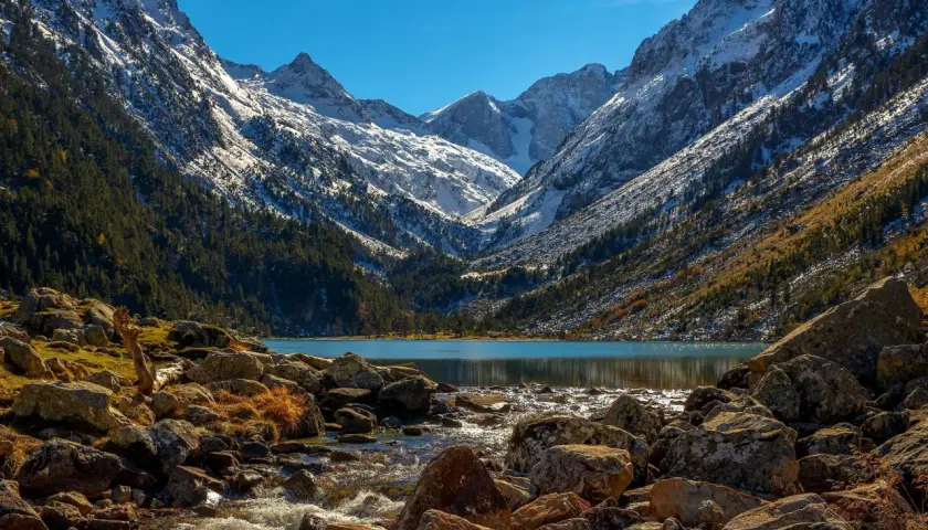Majestuosas montañas nevadas flanquean el sereno lac de Gaube, con un arroyo rocoso que desemboca en sus aguas turquesas.