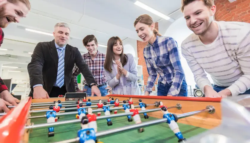 Colleagues laugh and play foosball, showcasing great employee engagement games.