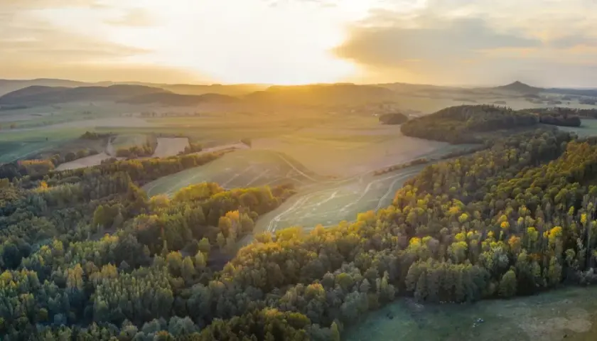 Zachód słońca nad pagórkami, gdzie przebiega szlak wygasłych wulkanów. Złote światło oświetla lasy i pola.