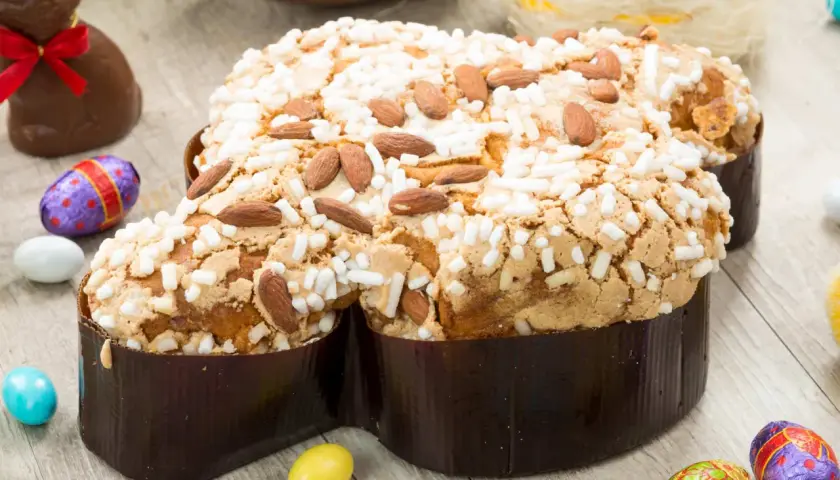Colomba pasquale ricetta: dolce soffice con mandorle e glassa croccante, circondata da uova di cioccolato e coniglietti.