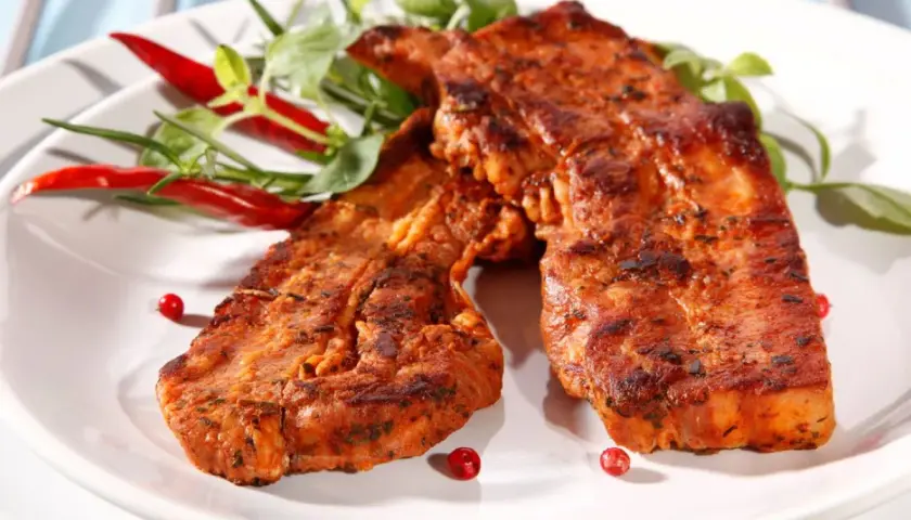 Dwa soczyste kawałki boczek z grilla, przyprawione i udekorowane papryczkami chili i zieleniną.