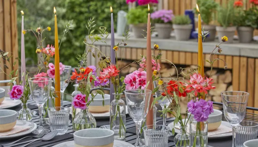 Tavola apparecchiata con candele colorate e fiori freschi, un'ispirazione per decorazioni estive fai da te.