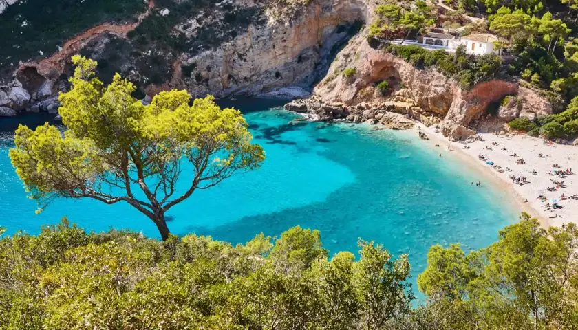 Una cala idílica con aguas turquesas y arena dorada, rodeada de acantilados y pinos. Un paraíso entre las mejores playas Comunidad Valenciana.