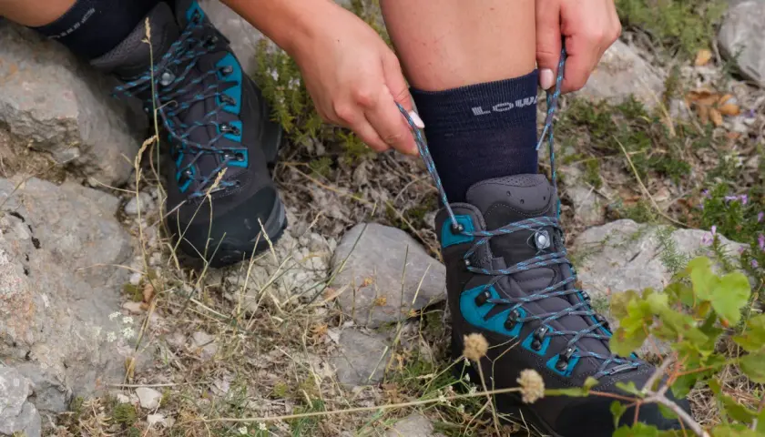 Hands tying the laces of a dark grey hiking boot with teal accents. Learn how to wear hiking boots for your next adventure.