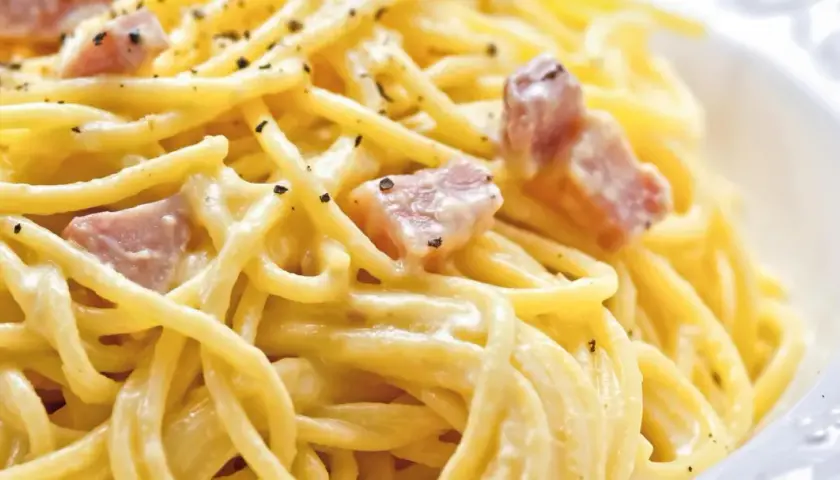 Ein Teller Spaghetti Carbonara, klassisch italienisch zubereitet mit cremiger Sauce und Speckwürfeln, bestreut mit schwarzem Pfeffer.