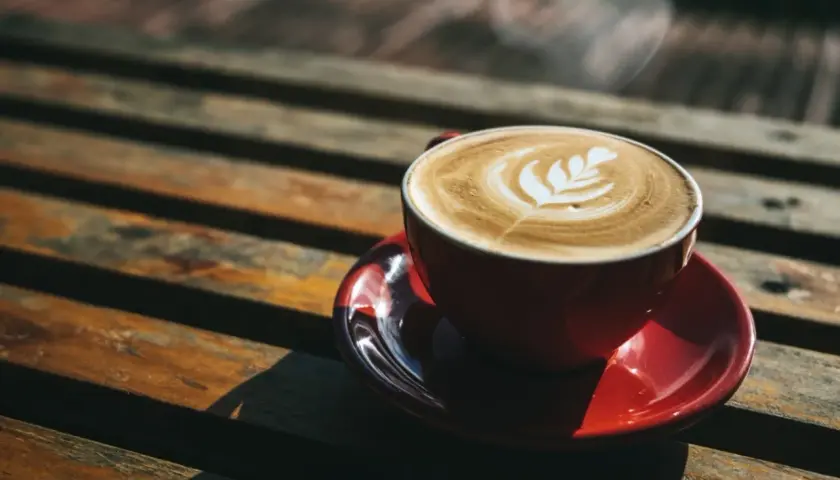 Czerwona filiżanka kawy latte z wzorem na piance, parująca na drewnianym stole. Czy kawę Inkę można pić wieczorem?