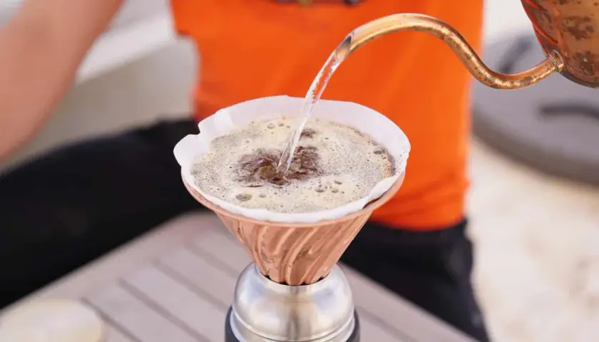 Heißes Wasser fließt aus einer Kupferkanne in einen Filter, um köstlichen Kaffee zu machen.