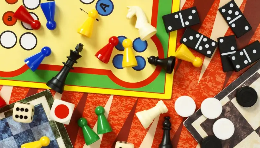Bunte Spielfiguren, Würfel, Dominosteine und Schachfiguren liegen verstreut. Eine bunte Mischung bekannter Brettspiele für endlosen Spielspaß.