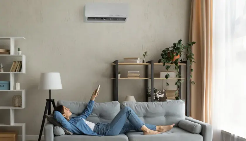 Mujer relajada en el sofá, usando el control remoto para programar el aire acondicionado y disfrutar de la temperatura perfecta.