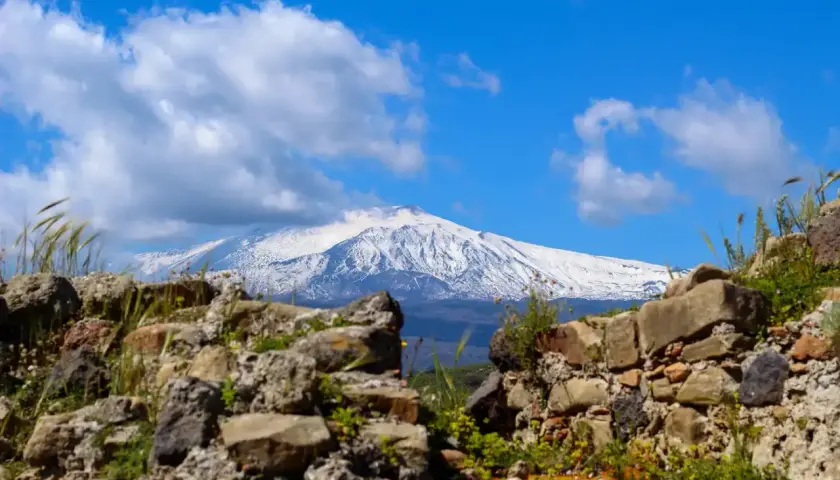 Rovine antiche incorniciano la maestosa vista dell'Etna innevato, un paesaggio iconico di Taormina.