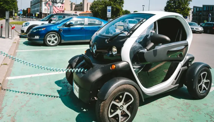 Mały, elektryczny pojazd, którym można jeździć bez prawa jazdy, ładuje się obok innych samochodów elektrycznych.