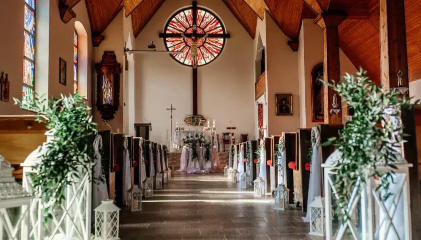 Piękna dekoracja kościoła na ślub samemu: ławki ozdobione zielenią i lampionami, ołtarz z kwiatami.
