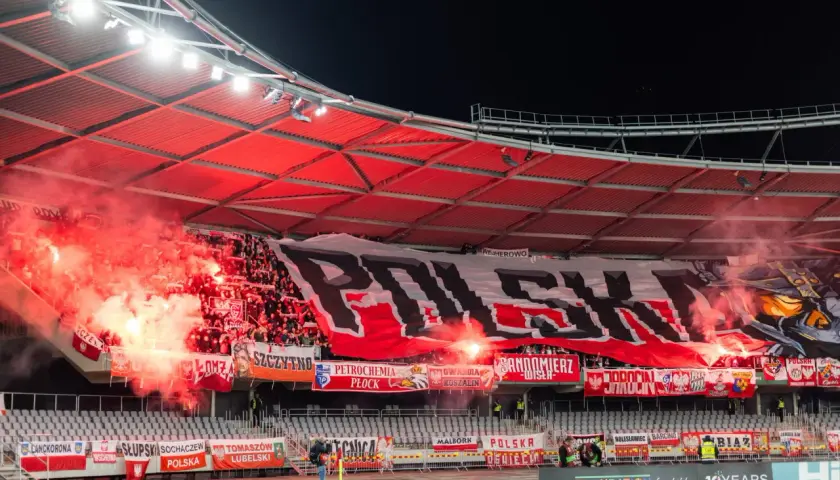 Tłum ultrasi na stadionie, odpalone race i ogromny transparent "POLSKA".