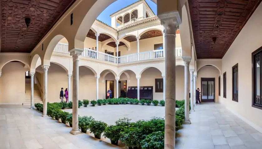 Wnętrze muzeum Picassa w Maladze, z dziedzińcem otoczonym arkadami, zdobionymi drewnianymi stropami i rzędami zieleni.