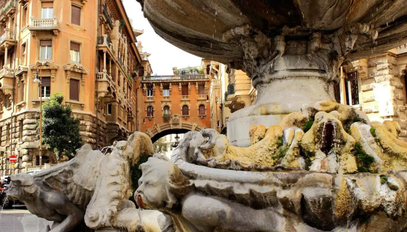 Fontana barocca a Roma Nord, con palazzi storici sullo sfondo e acqua che scorre tra le sculture.