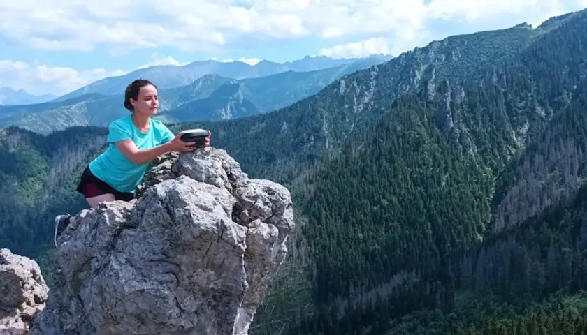 Kobieta na skale z urządzeniem w rękach, podziwia rozległą panoramę górską. Widok zapiera dech w piersiach, to prawdziwa przełęcz w tatrach wysokich.