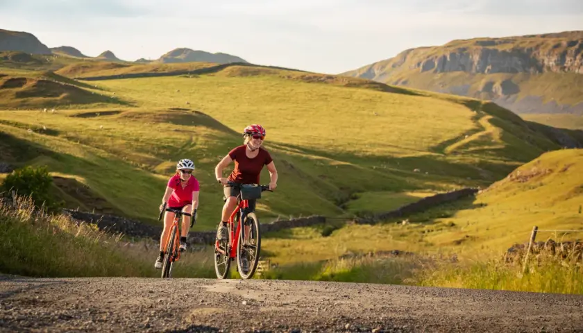 Two women enjoy a scenic ride on their bikes through rolling green hills, a perfect example of England bike tours.